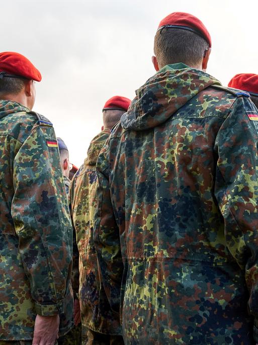 Soldaten der Bundeswehr stehen in Reih und Glied, gekleidet in Flecktarnuniformen und tragen rote sowie blaue Baretts.