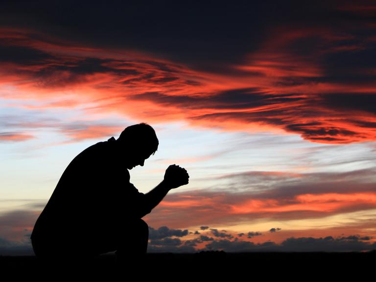 Ein Mann betet gegen den dramatischen Sonnenuntergang.