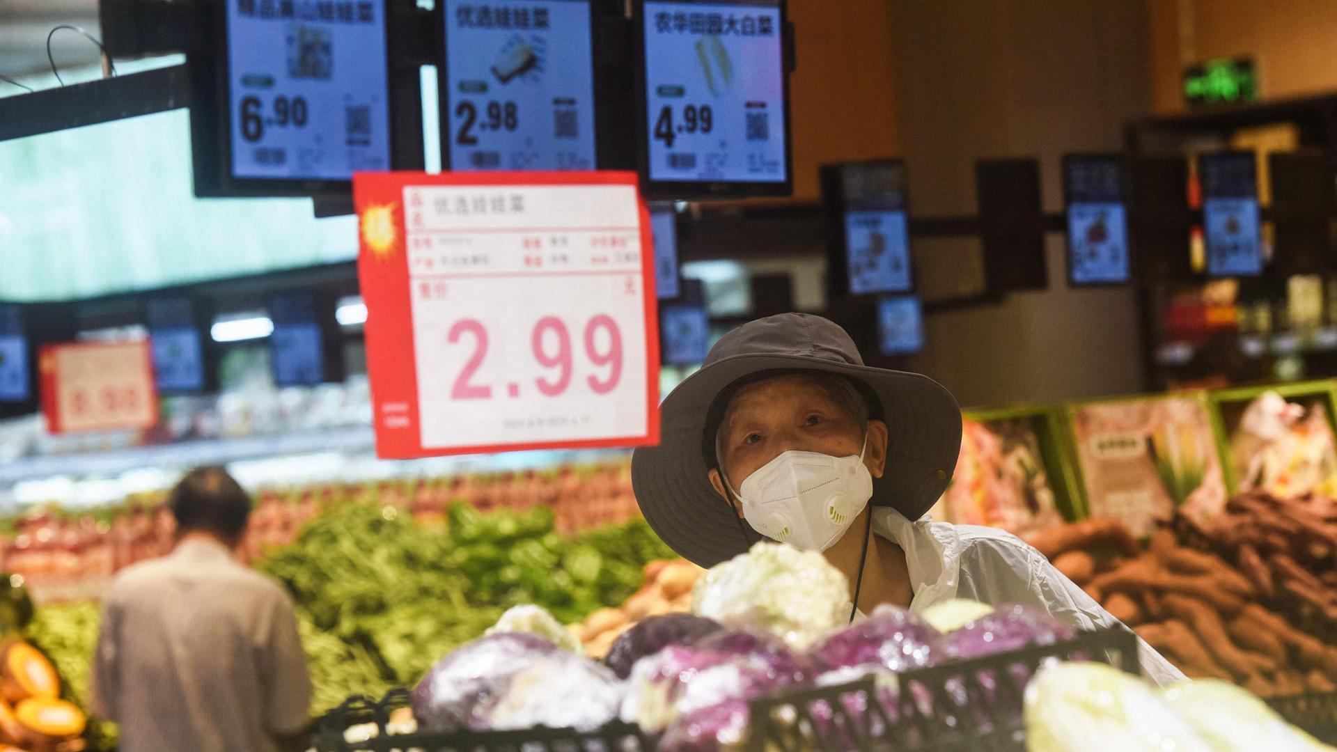 Eine Verkäuferin in China steht hinter ihrem Gemüsestand, hinter ihr ein großes Schild mit dem Preis 2,99. Eine Verkäuferin in China steht hinter ihrem Gemüsestand, hinter ihr ein großes Schild mit dem Preis 2,99.