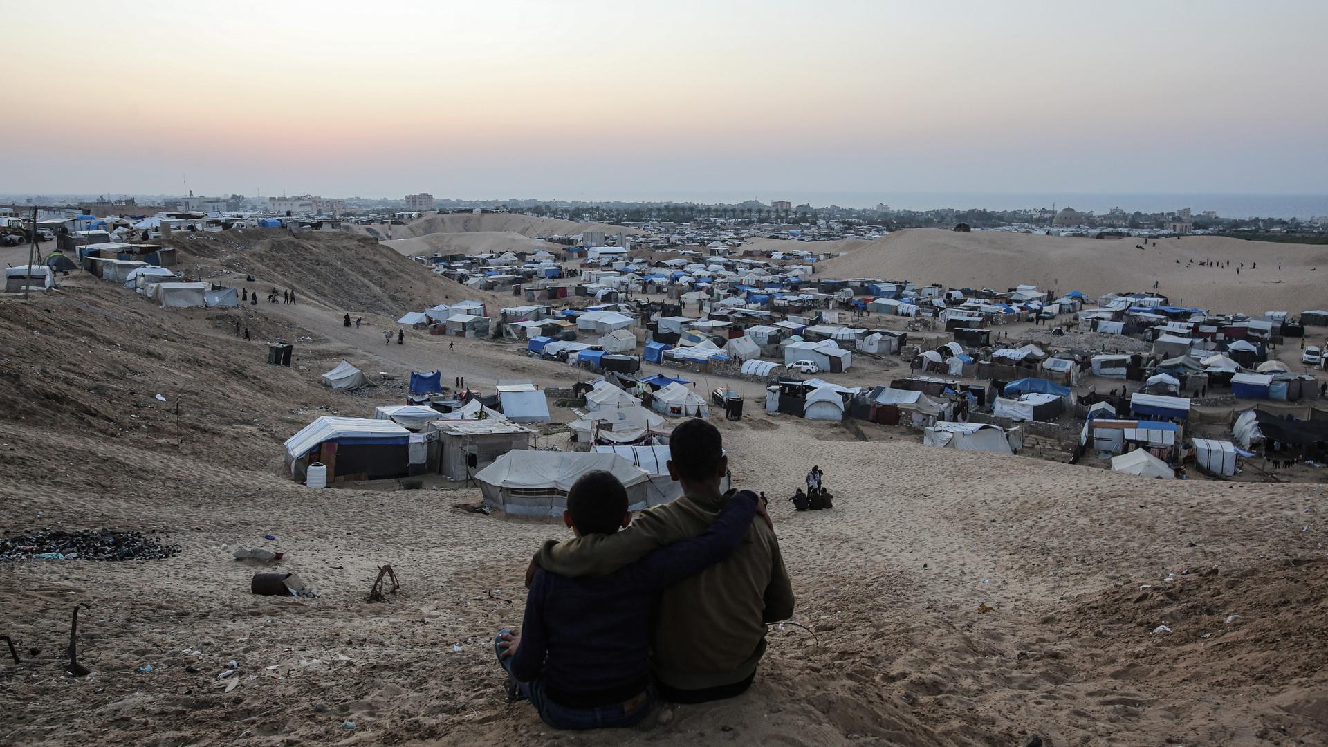 Blick über Zelte für Binnenflüchtlinge in der Mawasi-Region in Gaza, im Vordergrund sitzen zwei Personen nah nebeneinander.