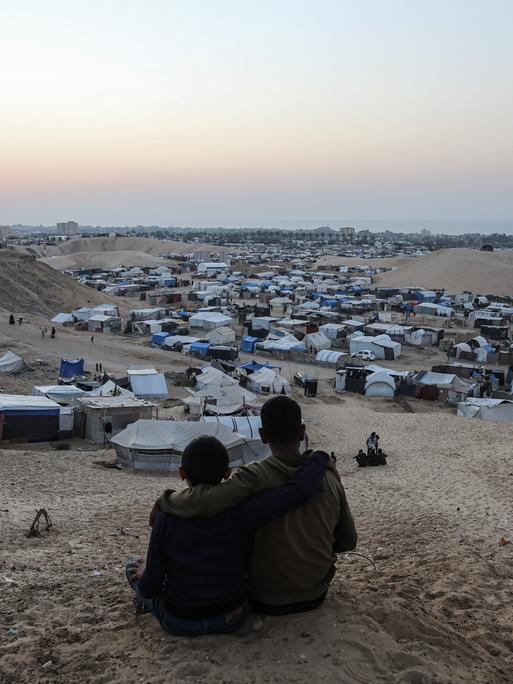 Blick über Zelte für Binnenflüchtlinge in der Mawasi-Region in Gaza, im Vordergrund sitzen zwei Personen nah nebeneinander.