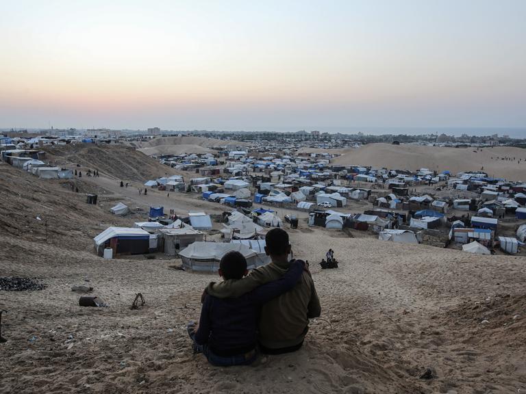 Blick über Zelte für Binnenflüchtlinge in der Mawasi-Region in Gaza, im Vordergrund sitzen zwei Personen nah nebeneinander.