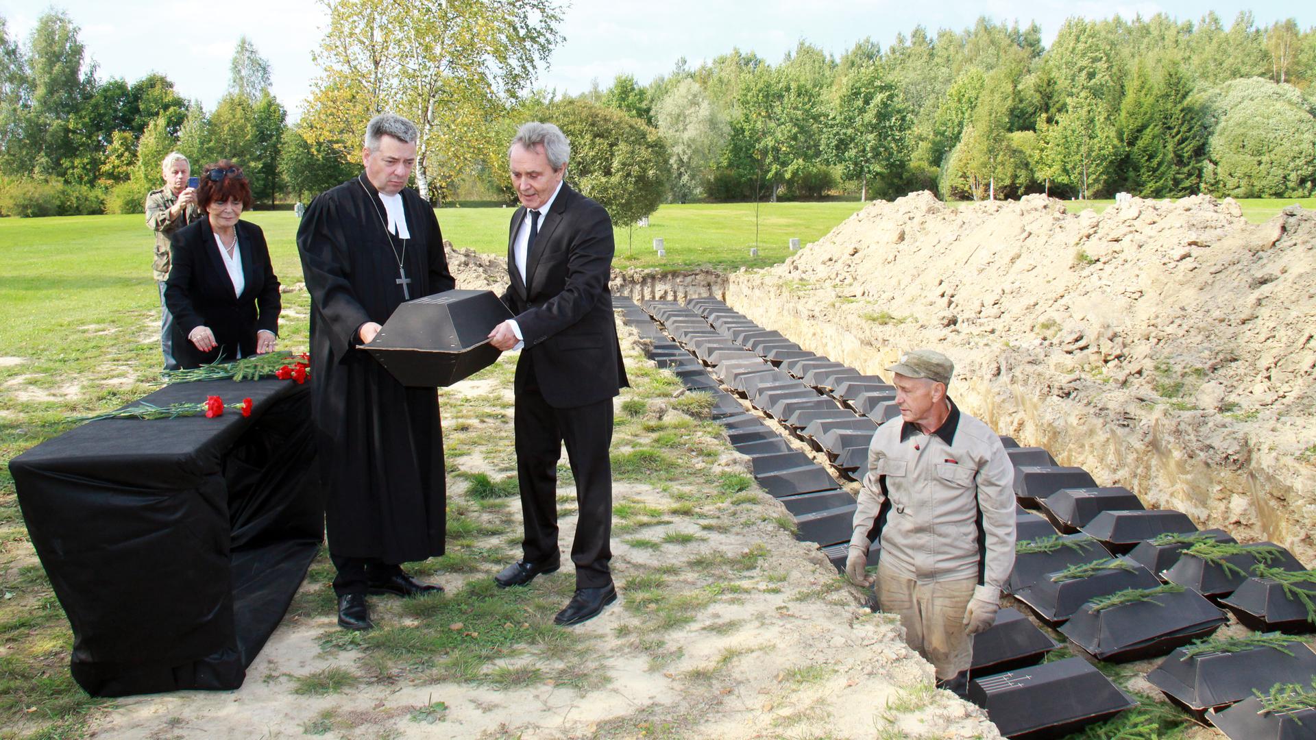 Hermann Krause (2.v.r.), Büroleiter des Volksbundes in Russland, und Michael Schwarzkopf (3.v.l.), Pastor der Petersburger Petrikirche, tragen einen schwarzen Pappsarg auf einem Soldatenfriedhof bei St. Petersburg. 