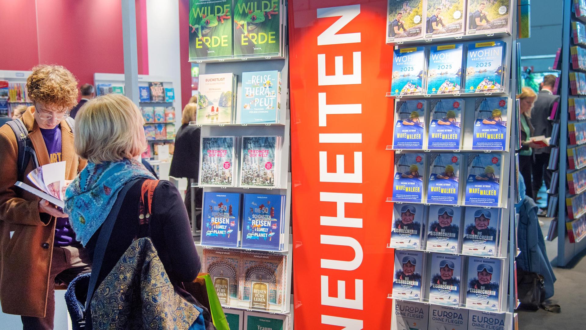 Die ersten Besucher schauen auf die Neuerscheinungen auf der Buchmesse. Sie stehen in einem großen Regal.