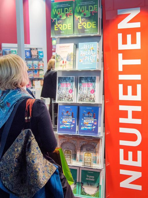 Die ersten Besucher schauen auf die Neuerscheinungen auf der Buchmesse. Sie stehen in einem großen Regal.