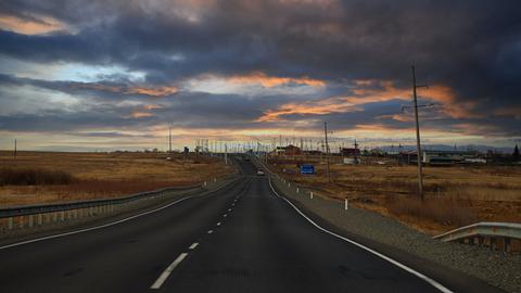 Eine Straße führt durch eine Steppe in einer bewölkten Abendstimmung. 