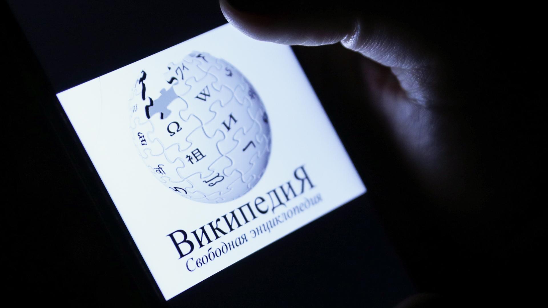 Auf einem Smartphone-Display ist das Logo der Online-Enzyklopädie Wikipedia, darunter der Name der Seite in kyrillischen Buchstaben und in russischer Sprache. Auf einem Smartphone-Display ist das Logo der Online-Enzyklopädie Wikipedia, darunter der Name der Seite in kyrillischen Buchstaben und in russischer Sprache.
