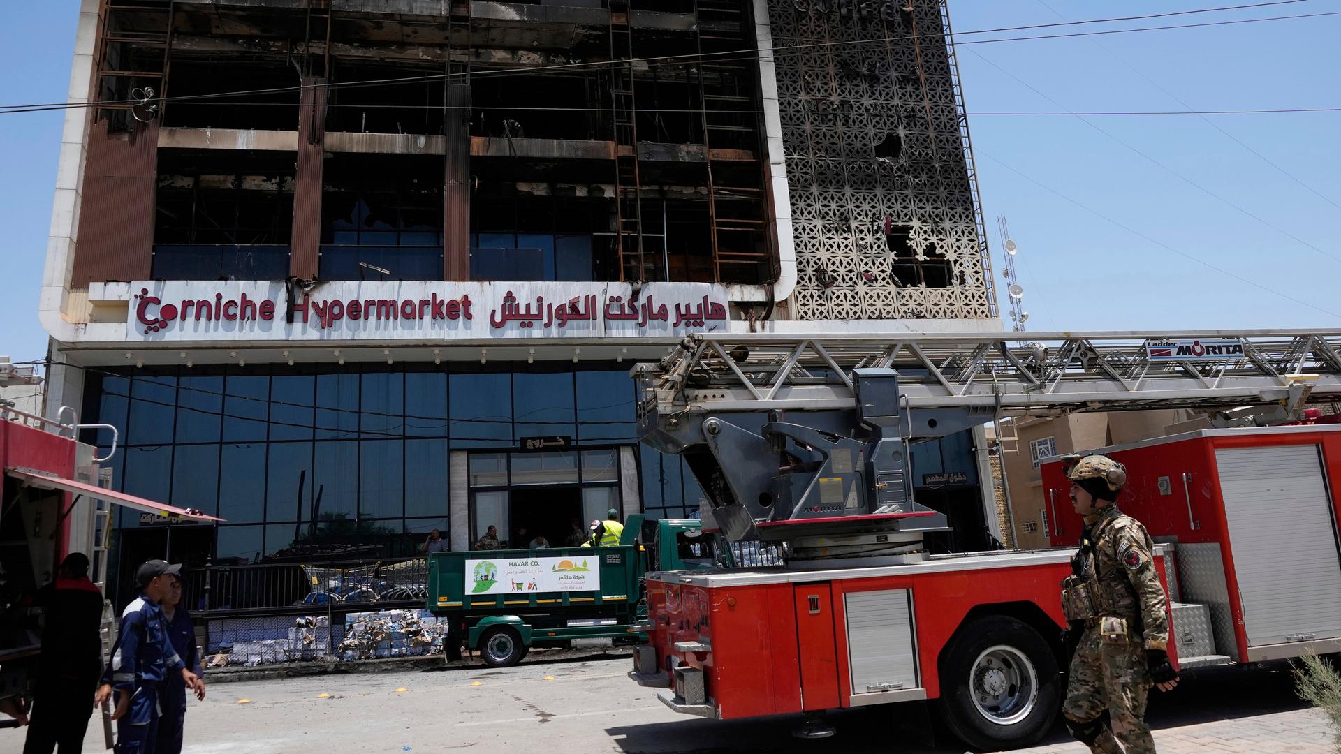 Feuerwehrleute stehen vor einem ausgebrannten Supermarktgebäude. Feuerwehrleute stehen vor einem ausgebrannten Supermarktgebäude.