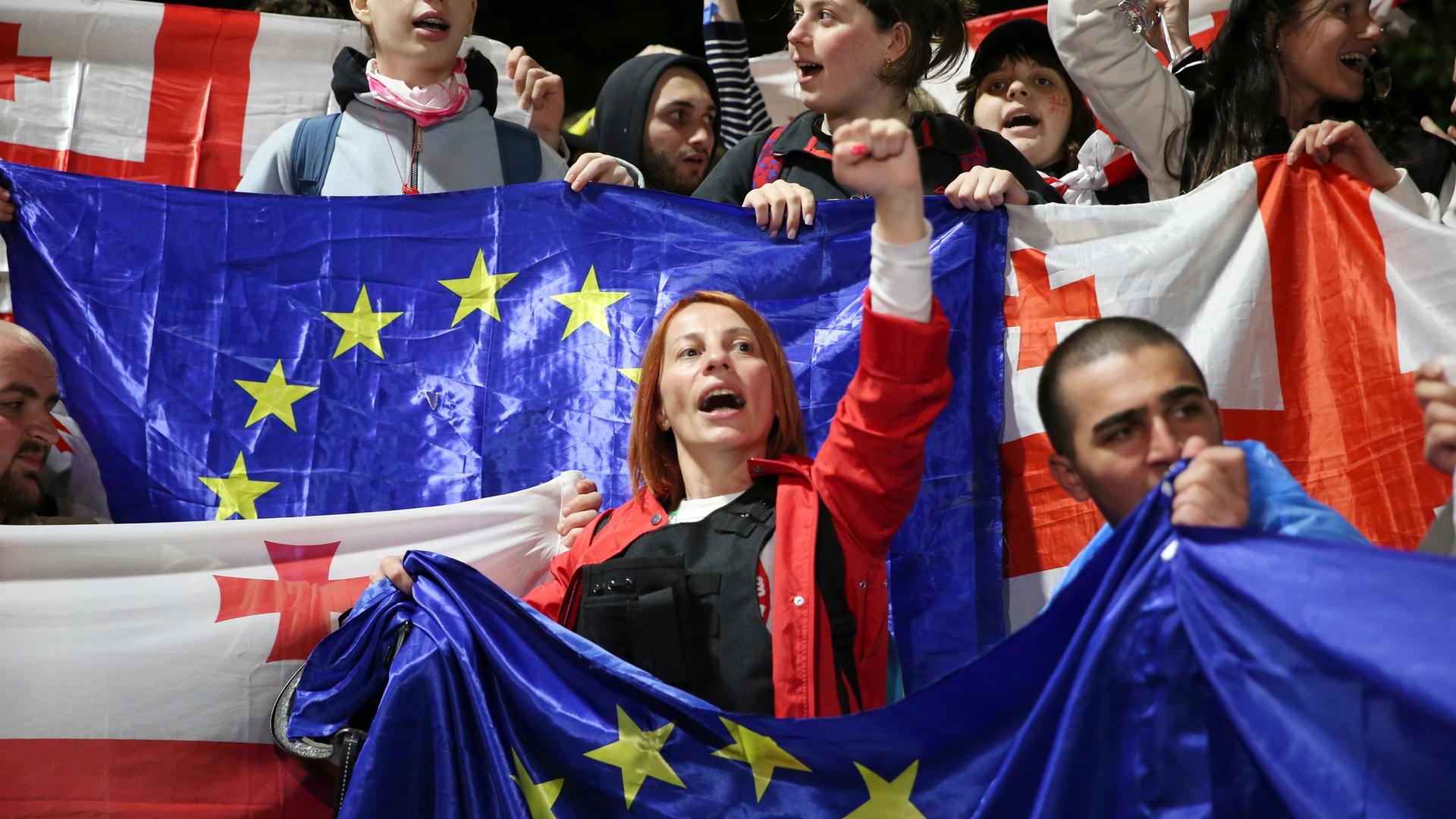 Demonstranten mit georgischen National- und EU-Flaggen rufen regierungsfeindliche Slogans in der Nähe des Parlamentsgebäudes während eines Protestes der Opposition gegen das „russische Gesetz“ im Zentrum von Tiflis, Georgien, am Montag, 13. Mai 2024. 