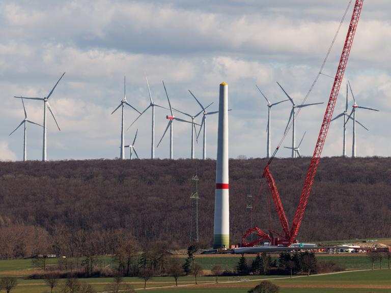 Zahlreiche Windkraftanlagen sind am 17.03.2025 in einem Windpark bei Borchen Etteln (Nordrhein-Westfalen) zu sehen, während im Vordergrund eine neue Windkraftanlage aufgebaut wird.