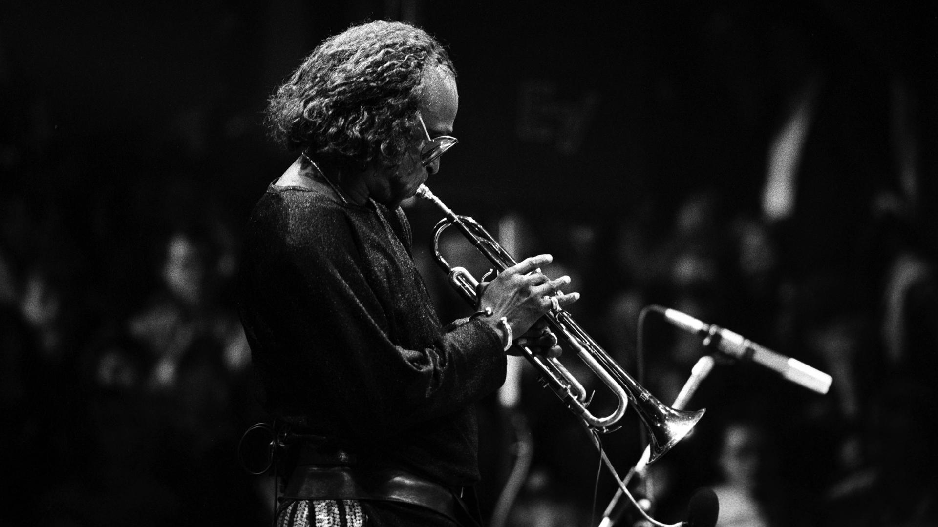 Ein Schwarz-Weiß-Foto zeigt Miles Davis im Profil mit Trompete auf der Bühne bei einem Konzert in Hamburg im Jahr 1986.
