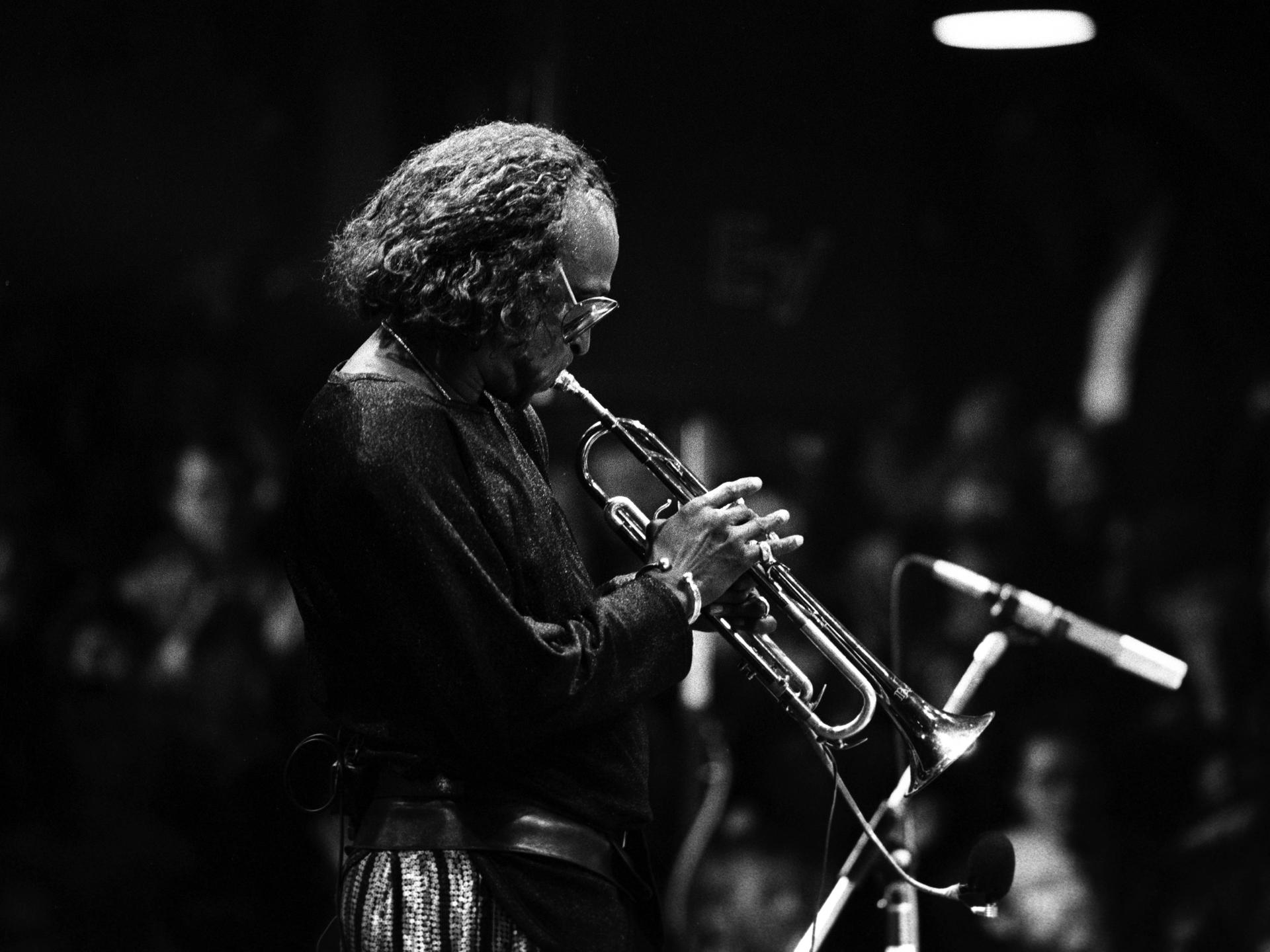Ein Schwarz-Weiß-Foto zeigt Miles Davis im Profil mit Trompete auf der Bühne bei einem Konzert in Hamburg im Jahr 1986.