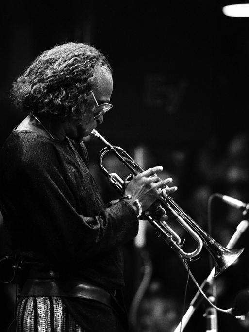 Ein Schwarz-Weiß-Foto zeigt Miles Davis im Profil mit Trompete auf der Bühne bei einem Konzert in Hamburg im Jahr 1986.