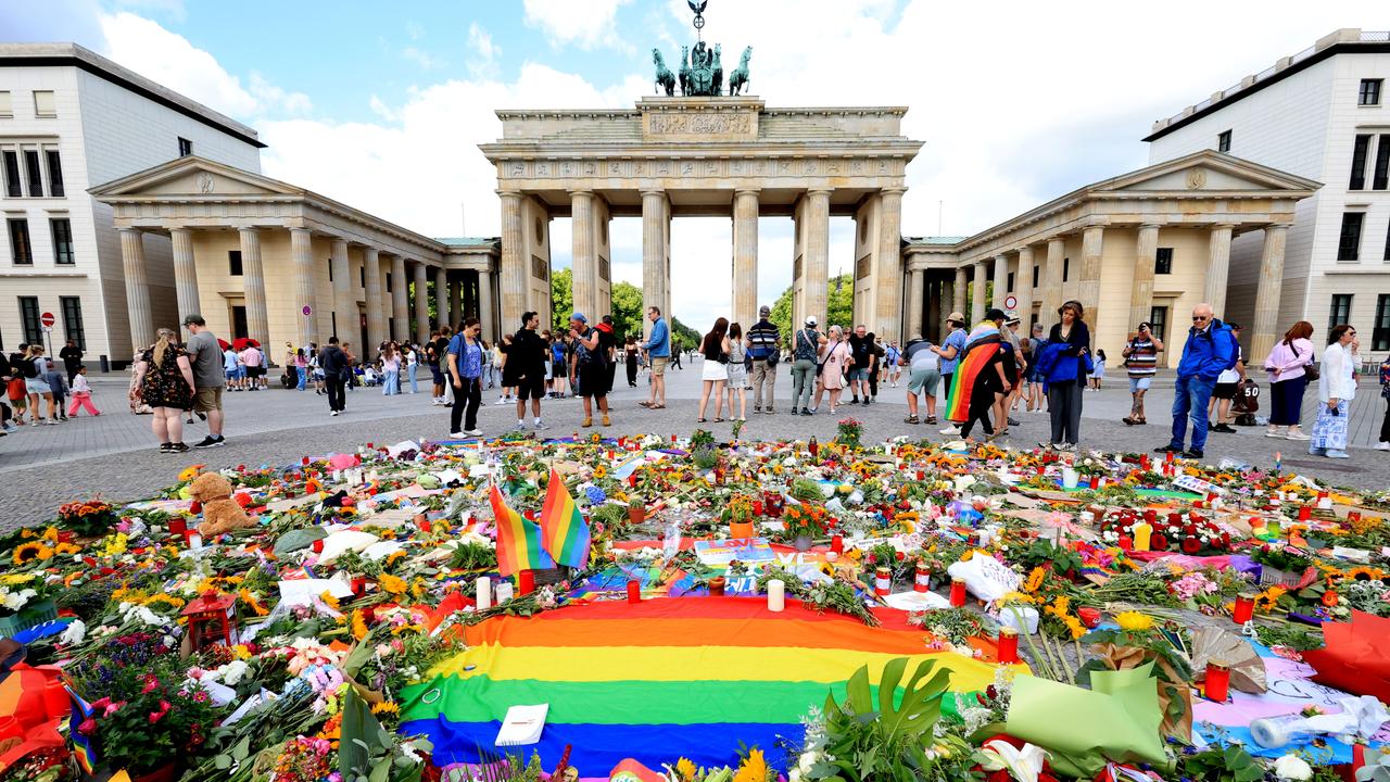 Vor dem Brandenburger Tor in Berlin liegen viele Blumen, Kerzen und eine Regenbogen-Fahne für die Opfer des Terroranschlags vom 25.07.2026 beim CSD-Berlin 