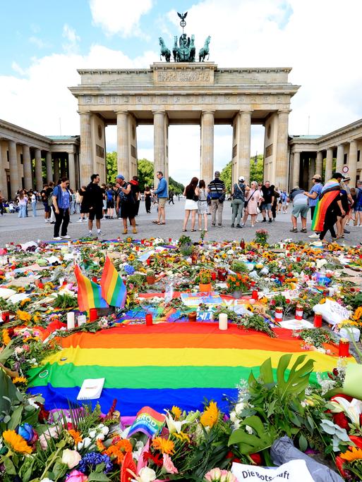 Vor dem Brandenburger Tor in Berlin liegen viele Blumen, Kerzen und eine Regenbogen-Fahne für die Opfer des Terroranschlags vom 25.07.2026 beim CSD-Berlin 