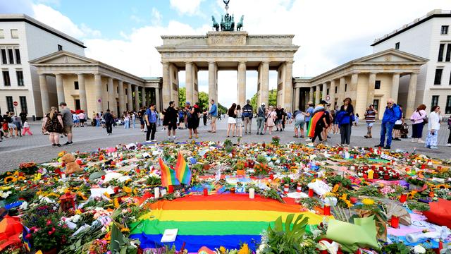 Vor dem Brandenburger Tor in Berlin liegen viele Blumen, Kerzen und eine Regenbogen-Fahne für die Opfer des Terroranschlags vom 25.07.2026 beim CSD-Berlin 