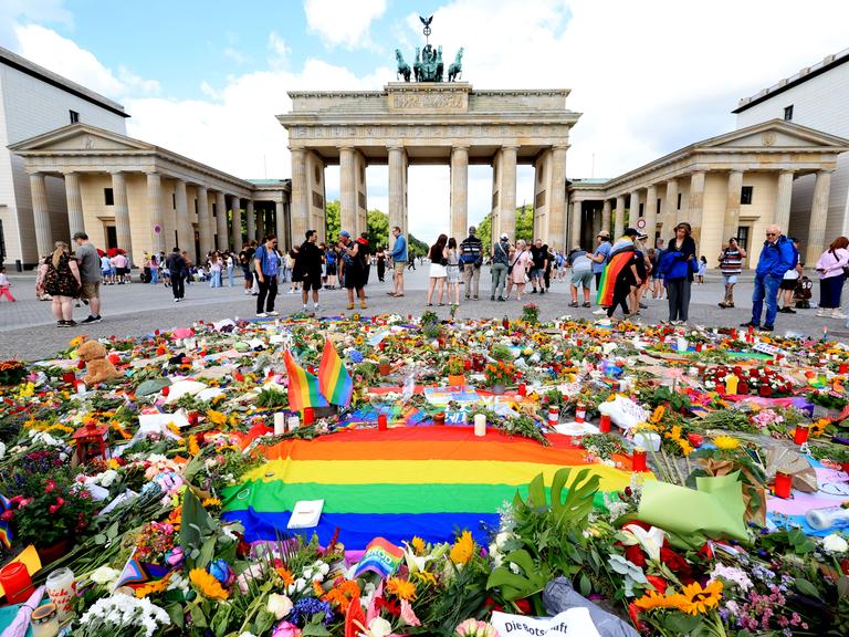 Vor dem Brandenburger Tor in Berlin liegen viele Blumen, Kerzen und eine Regenbogen-Fahne für die Opfer des Terroranschlags vom 25.07.2026 beim CSD-Berlin 