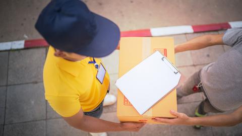 Im direkten Gespräch mit seiner Kundschaft begreift sich Paketzusteller Joël als Lebenshelfer. Zu sehen: Aufnahme von oben -  ein Paketzusteller überreicht ein Paket. 