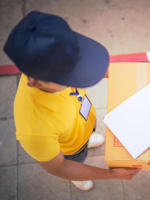 Im direkten Gespräch mit seiner Kundschaft begreift sich Paketzusteller Joël als Lebenshelfer. Zu sehen: Aufnahme von oben -  ein Paketzusteller überreicht ein Paket. 
