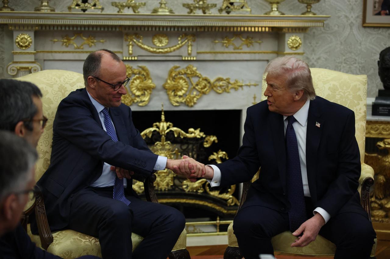 Bundeskanzler Merz und Präsident Trump sitzen nebeneinander auf zwei Sesseln und geben sich die Hand.