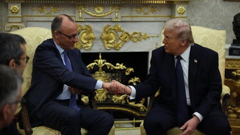 Bundeskanzler Merz und Präsident Trump sitzen nebeneinander auf zwei Sesseln und geben sich die Hand.