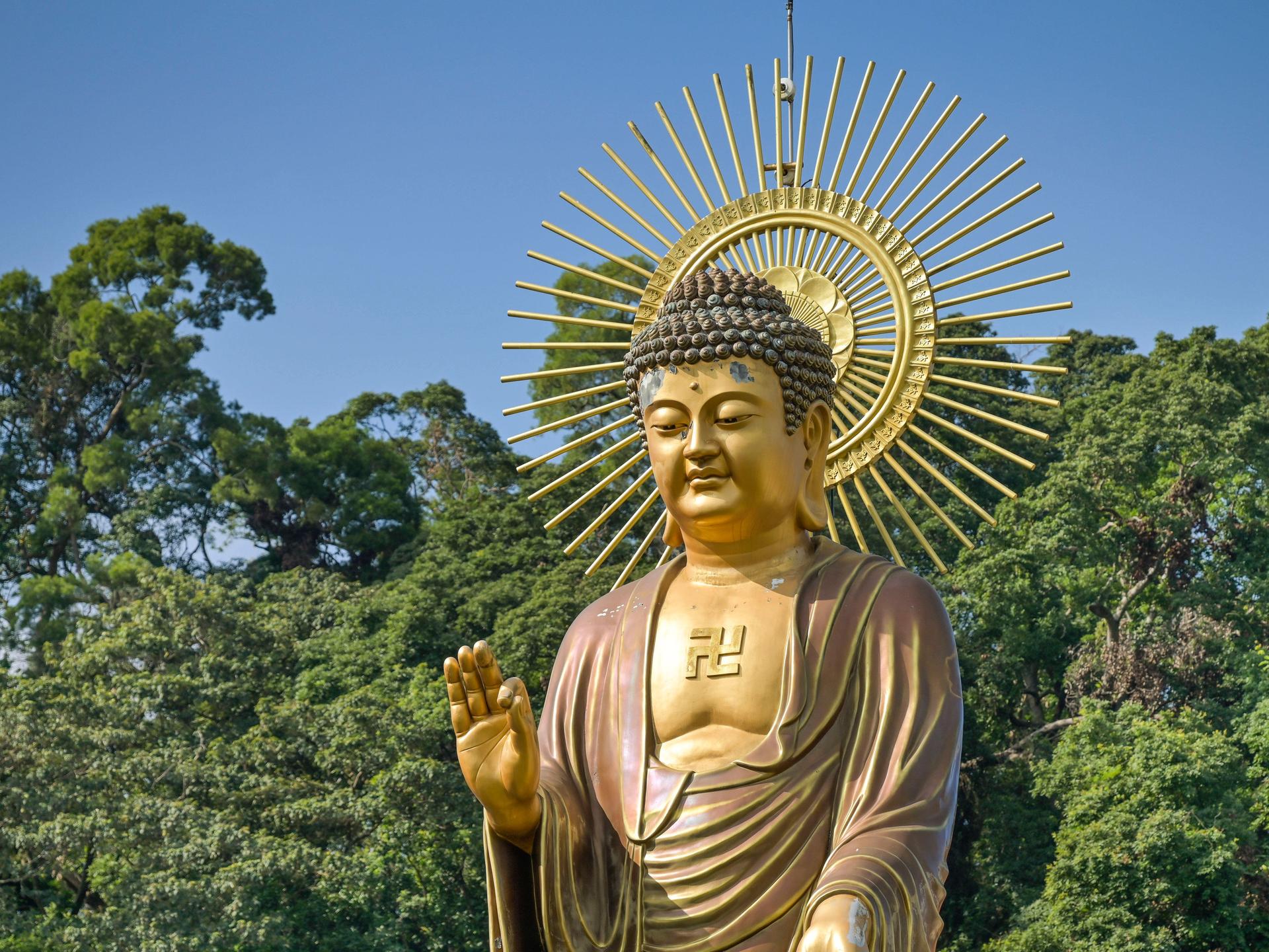 Eine große Buddhastatue steht in Taiwan vor blauem Himmel und tiefgrünen Baumkronen.