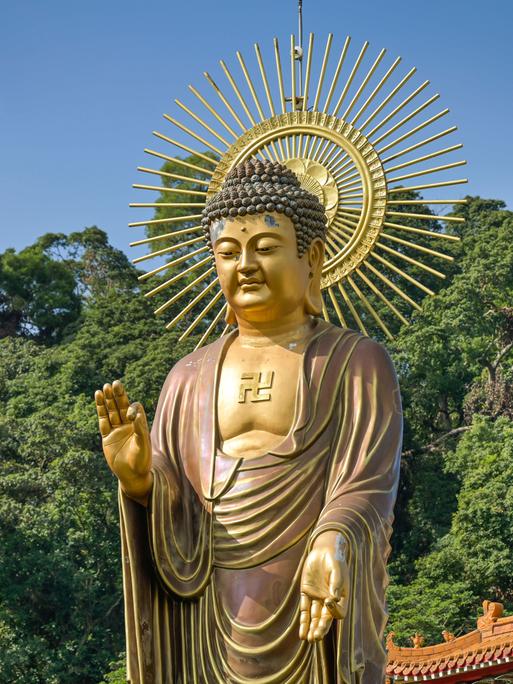 Eine große Buddhastatue steht in Taiwan vor blauem Himmel und tiefgrünen Baumkronen.