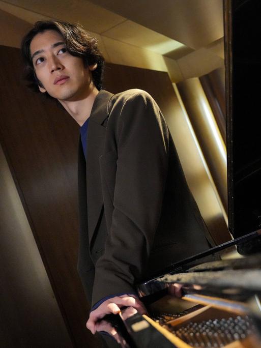 Der japanische Pianist ist schräg über einen Flügel hinweg mit schrägen Perspektiven aufgenommen.