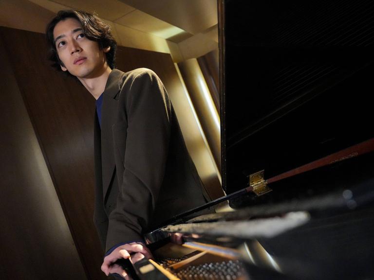 Der japanische Pianist ist schräg über einen Flügel hinweg mit schrägen Perspektiven aufgenommen.