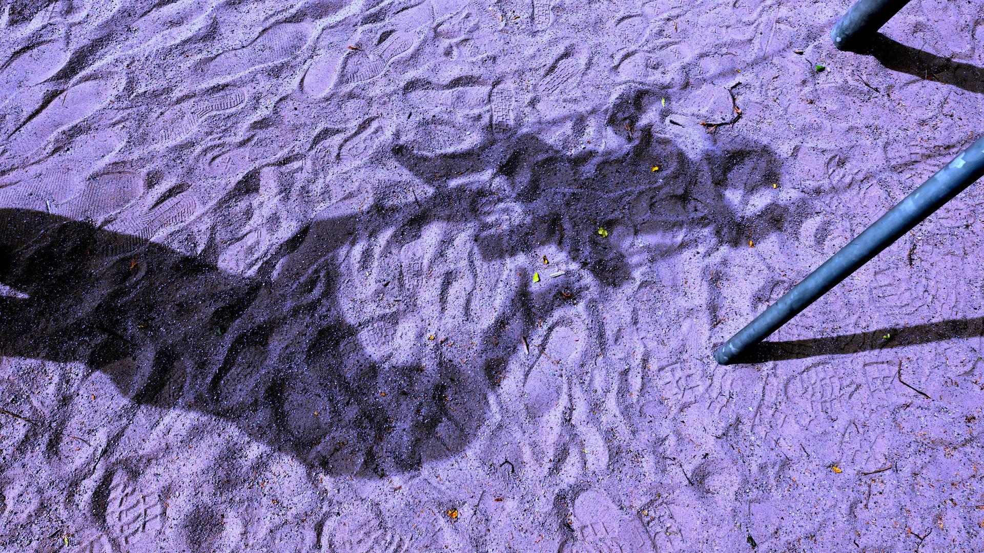 Silhouette eines Kindes auf einer Schaukel ist auf dem Sand eines Spielplatzes zu sehen. 
