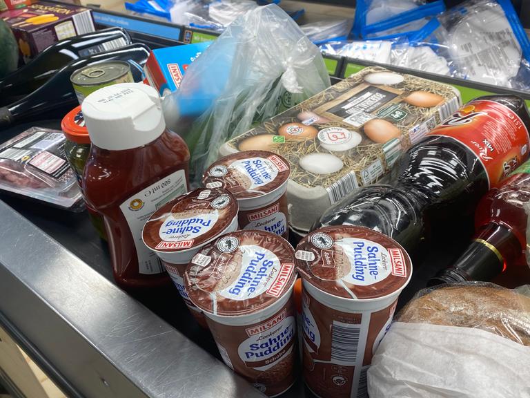 Verschiedene Lebensmittel liegen auf einem Kassenband an einer Supermarktkasse.