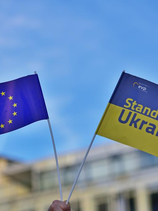 Eine EU-Fahne neben einer ukrainischen Fahne mit der Aufschrift "Stand with Ukraine".
