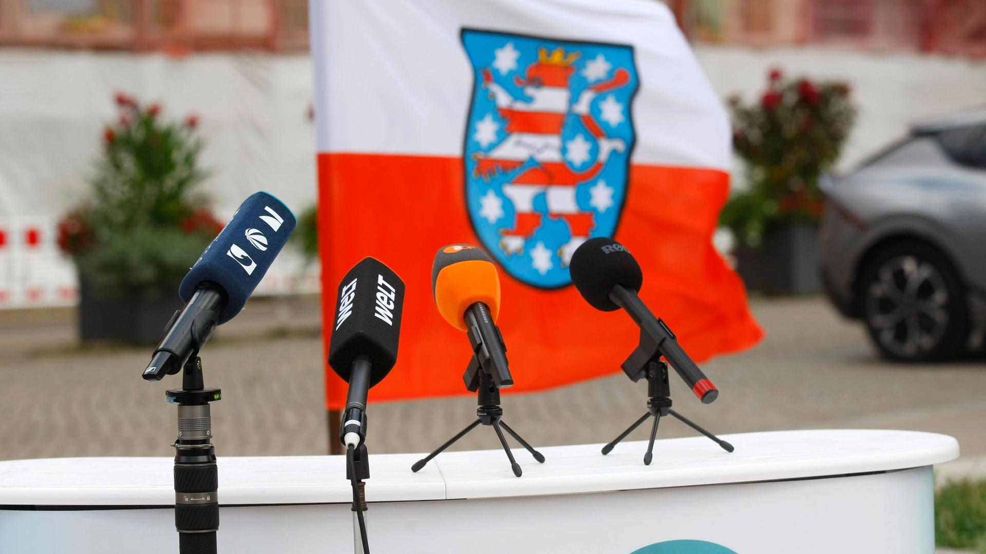 Die Mikrofone verschiedener Medienanstalten stehen auf einem Podest vor der thüringischen Landesflagge.