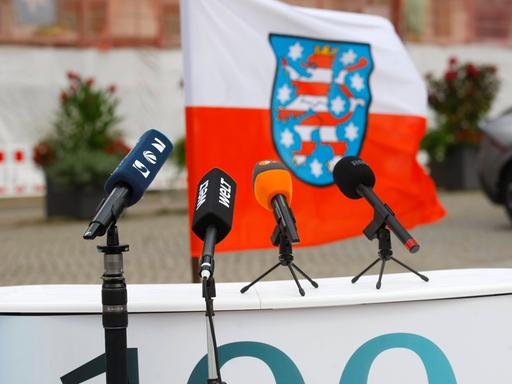 Die Mikrofone verschiedener Medienanstalten stehen auf einem Podest vor der thüringischen Landesflagge.