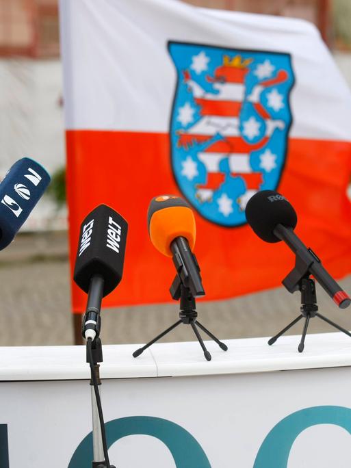 Die Mikrofone verschiedener Medienanstalten stehen auf einem Podest vor der thüringischen Landesflagge.