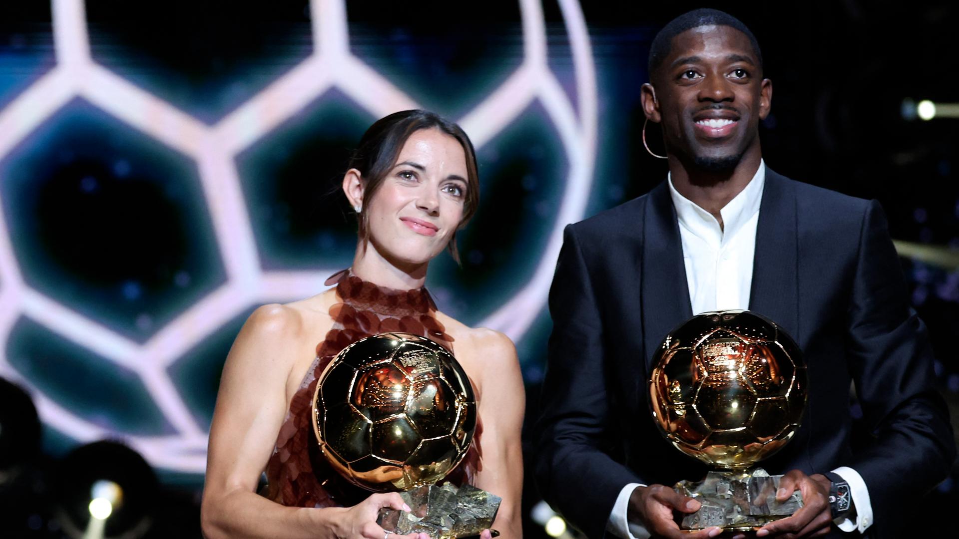 Fußballerin Bonmati und Fußballer Dembele stehen gemeinsam auf der Bühne. Sie halten stolz einen goldenen Fußball vor sich. Das  Das Bild ist von einer Preis-Verleihung aus dem Monat September.