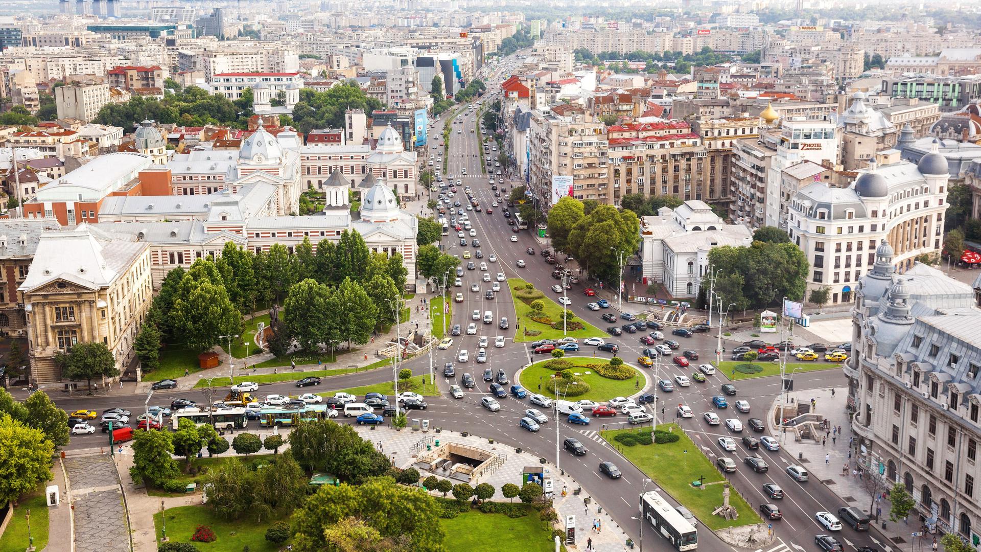 Sicht ins Stadtzentrum von Bukarest, ein großer Kreisverkehr mit vielen Autos neben Gebäuden