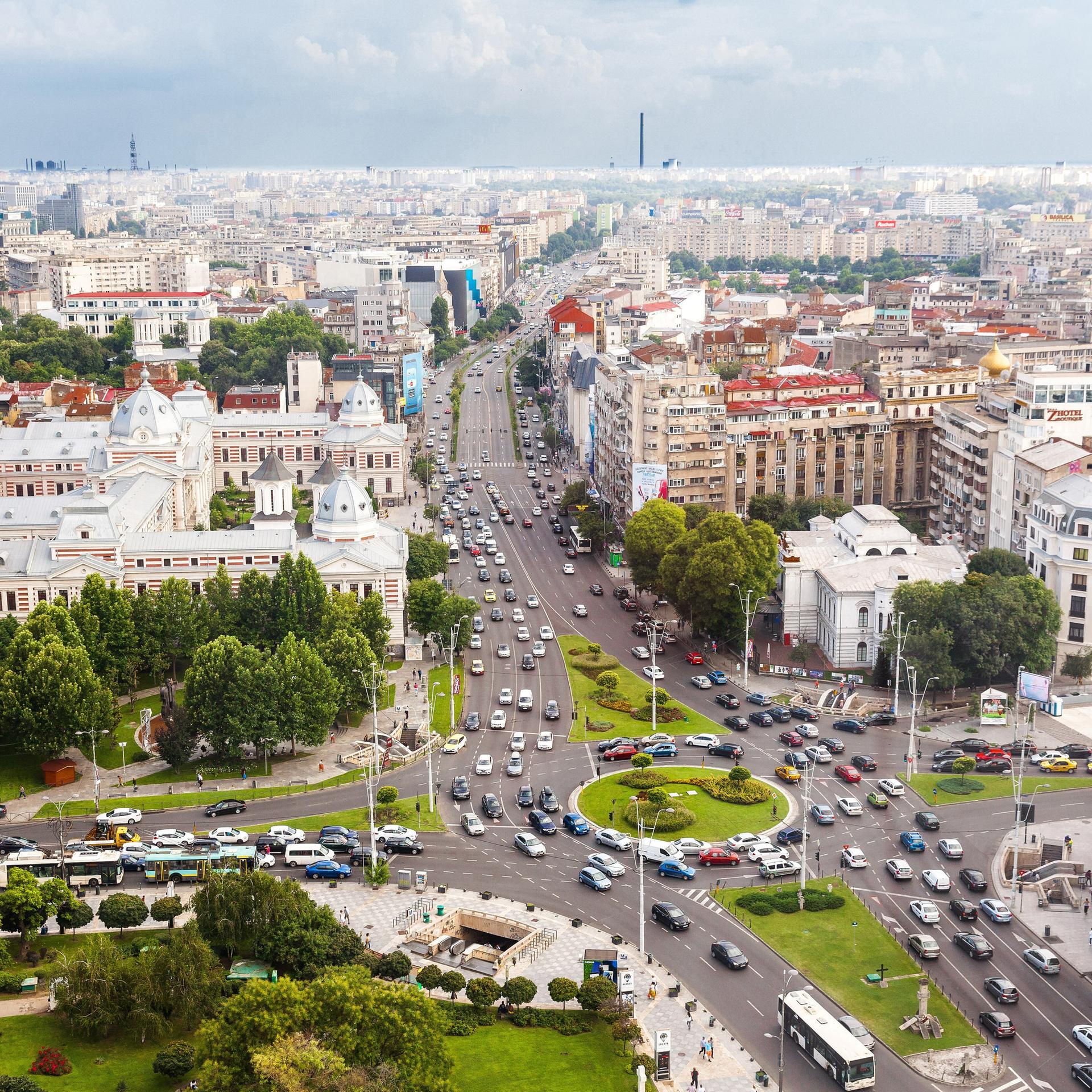 Sicht ins Stadtzentrum von Bukarest, ein großer Kreisverkehr mit vielen Autos neben Gebäuden