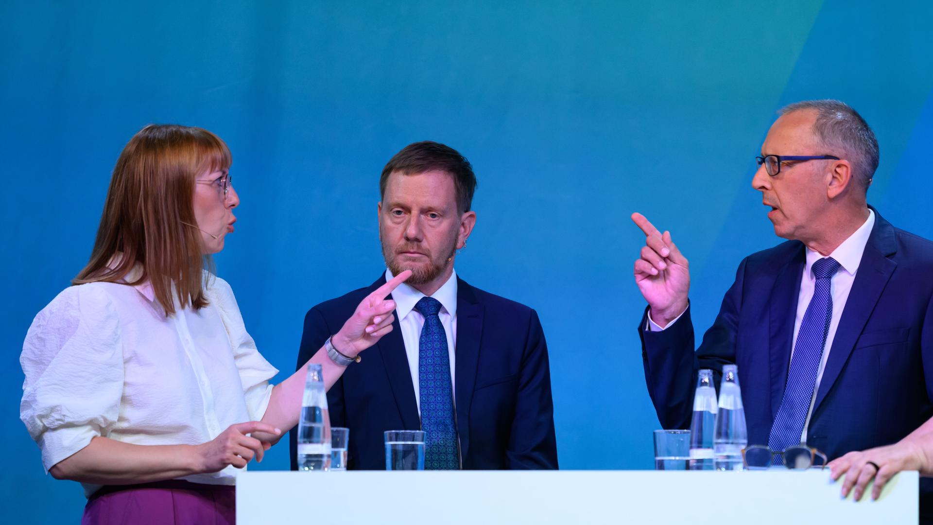 Katja Meier (Bündnis90/Die Grünen, l-r), Justizministerin von Sachsen,Michael Kretschmer (CDU), Ministerpräsident von Sachsen und Jörg Urban, Vorsitzender der AfD in Sachsen, stehen an einem Tisch und diskutieren miteinander.