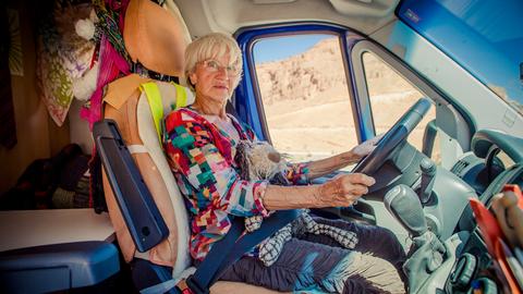 Gisela sitzt am Steuer Ihres Kleintransporters und schaut Richtung Betrachter.