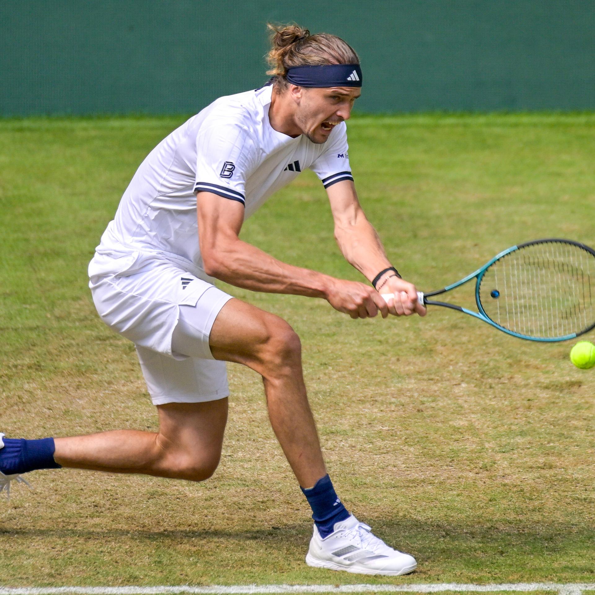 Alexander Zverev trägt Tenniskleidung und hat einen Tennisschläger in der Hand, mit dem er sich nach einem heranfliegenden Ball streckt.