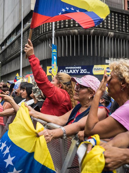 Unterstützerinnen und Unterstützer des bisherigen Staatschefs von Venezuela Nicolás Maduro stehen nach dessen Entführung durch die USA bei einer Demonstration beieinander und schwenken venezolanische Flaggen. 