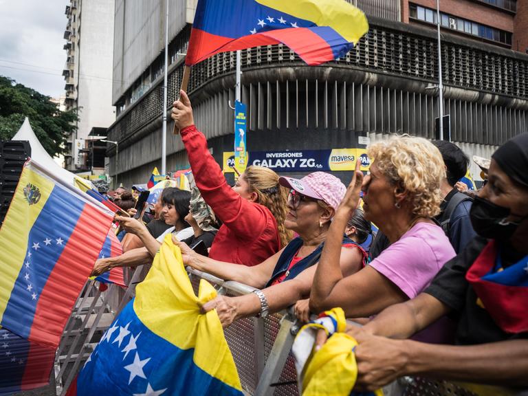 Unterstützerinnen und Unterstützer des bisherigen Staatschefs von Venezuela Nicolás Maduro stehen nach dessen Entführung durch die USA bei einer Demonstration beieinander und schwenken venezolanische Flaggen. 