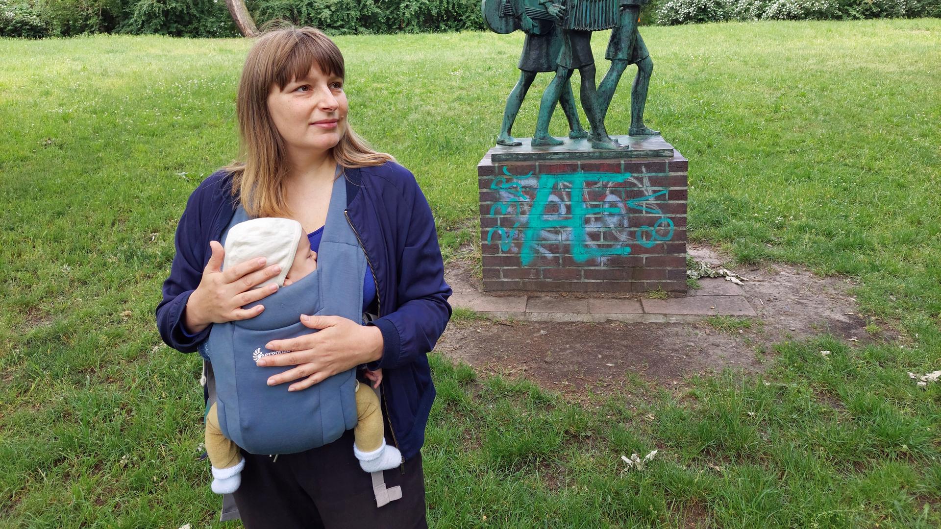 Eine junge Frau mit einem Baby im Tragetuch in einem Park