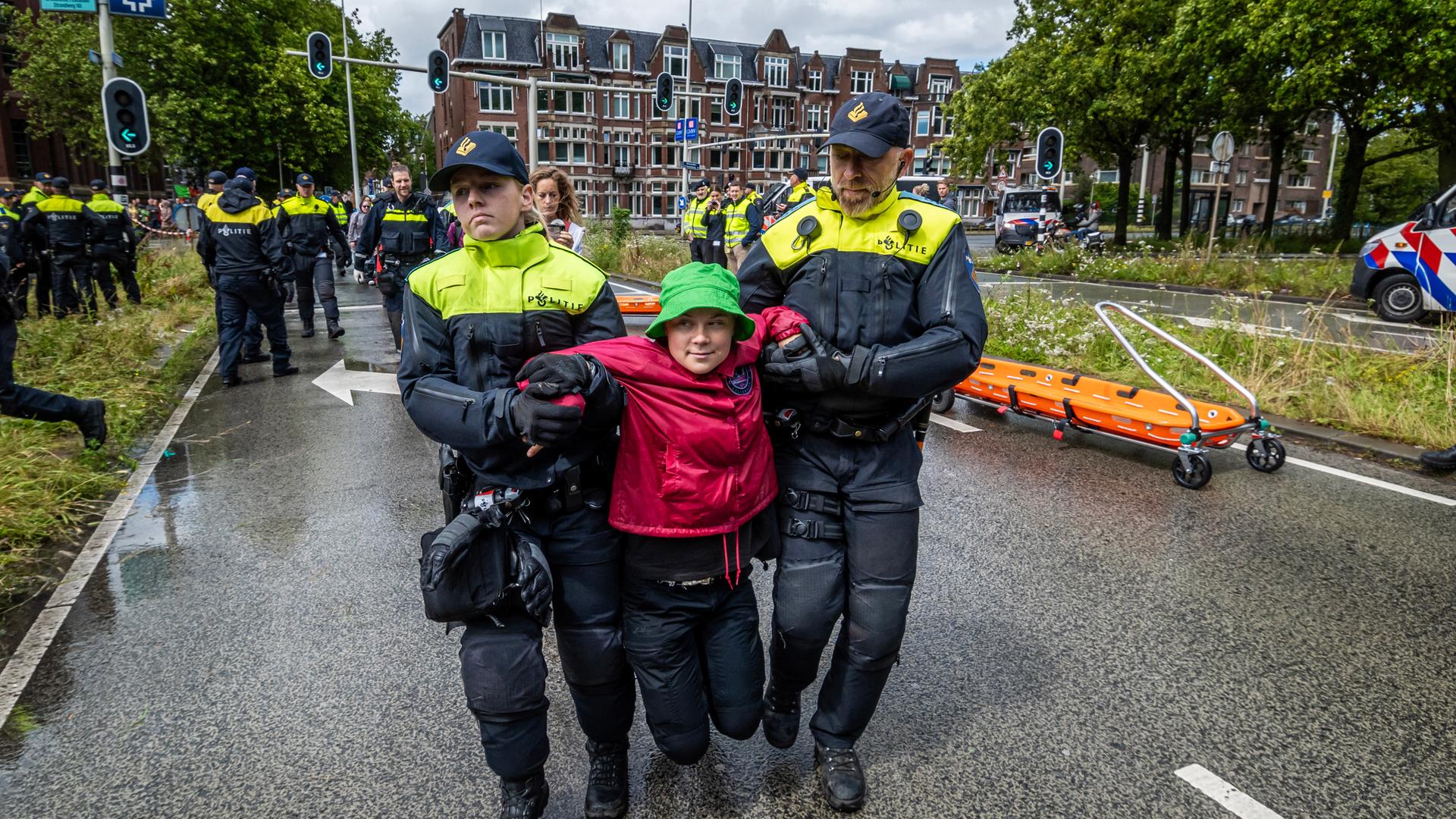 Zwei Polizisten haben Greta Thunberg unter die Arme gefasst und tragen sie eine Straße entlang. 