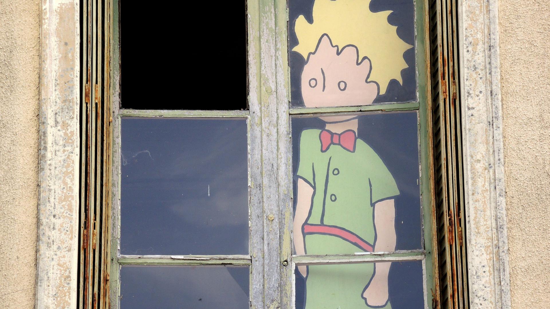 Die Figur des "Kleinen Prinzen" mit gelben Haaren und grüner Kleidung blickt hinter einem Fenster nach draußen.