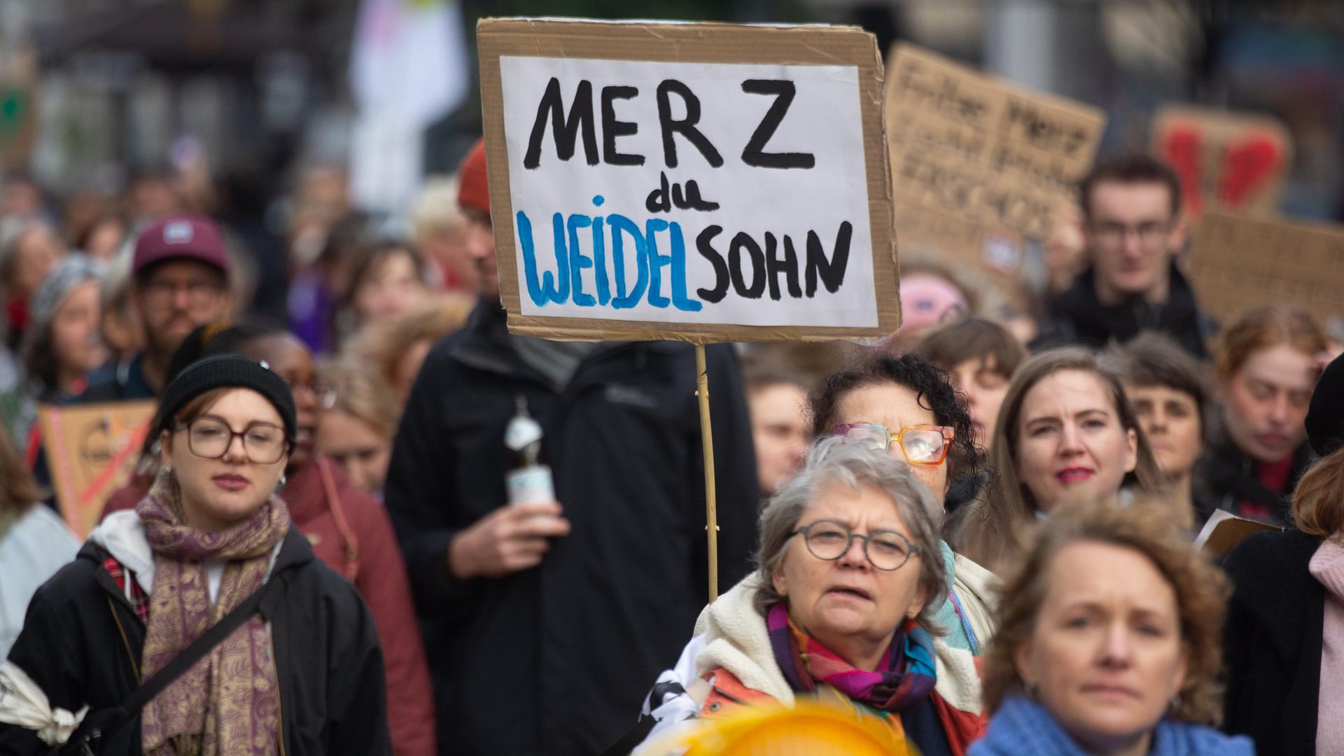 Proteste gegen Bundeskanzler Friedrich Merz und seine Stadtbild-Äußerung: Auf einer Demo wird ein Schild mit der Aufschrift "Merz du Weidelsohn" hochgehalten.
