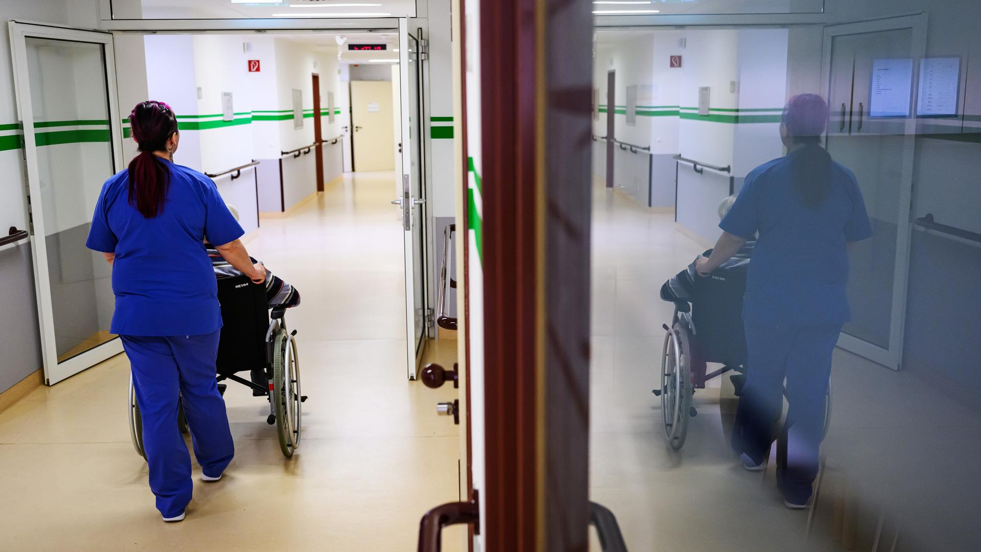 Eine Pflegerin der Geriatrie im DRK-Krankenhaus Chemnitz schiebt einen Patienten im Rollstuhl über die Station.