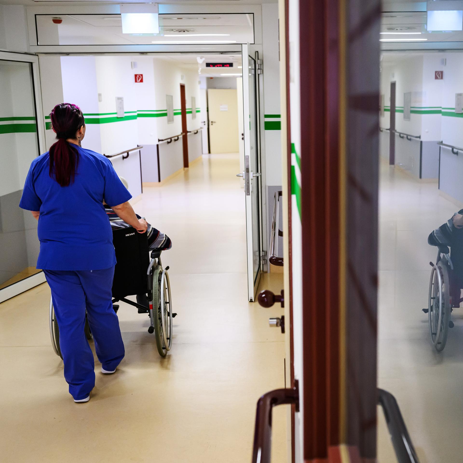 Eine Pflegerin der Geriatrie im DRK-Krankenhaus Chemnitz schiebt einen Patienten im Rollstuhl über die Station.