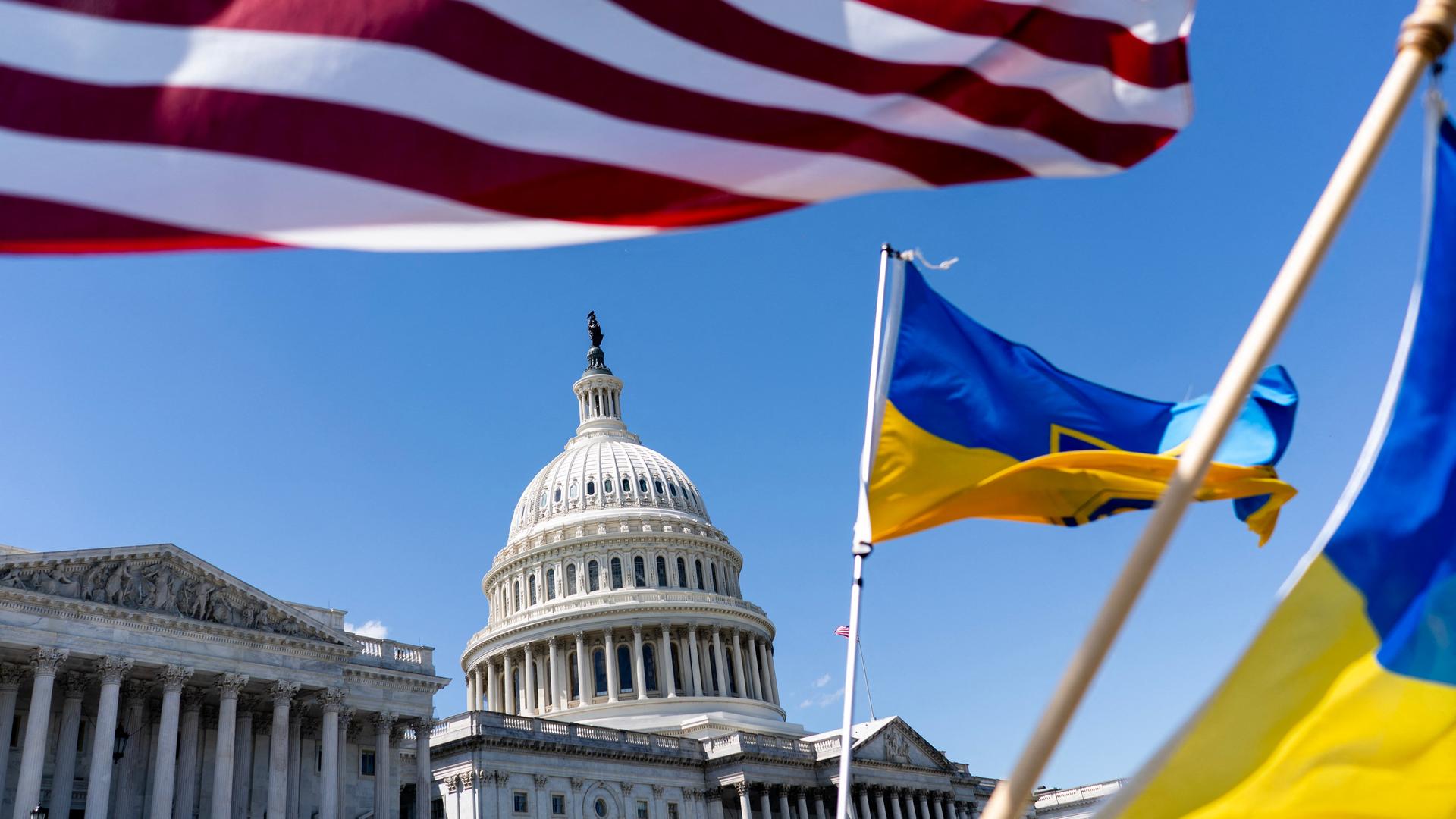 Die ukrainische und die US-amerikanische Flagge wehen vor dem Kapitol in Washington, im Hintergrund blauer Himmel.